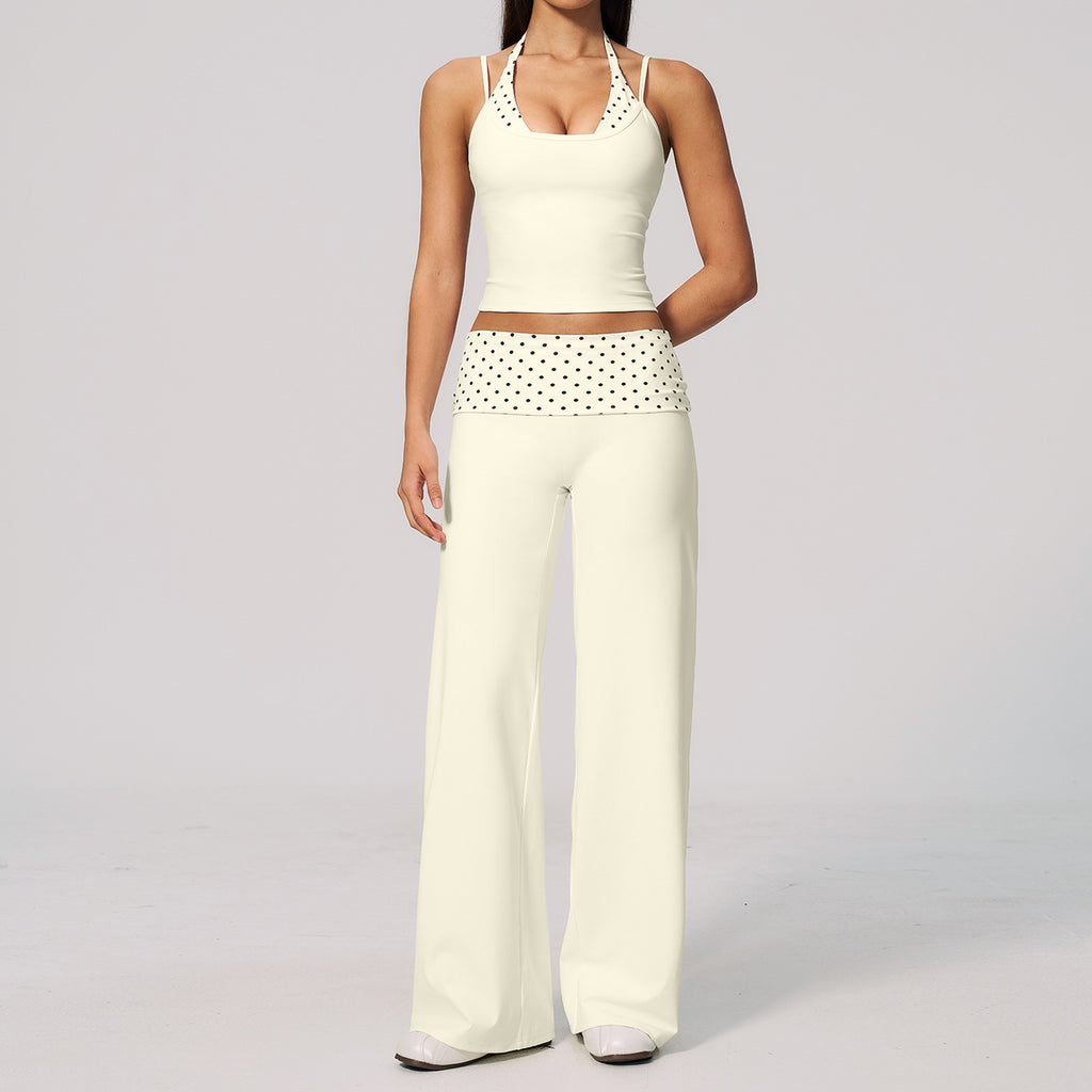 A model wearing a cream-colored two-piece lounge set consisting of a halter crop top with crochet detailing and matching wide-leg pants with a polka-dot waistband, set against a plain light gray background.