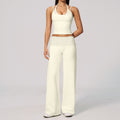 A model wearing a cream-colored two-piece lounge set consisting of a halter crop top with crochet detailing and matching wide-leg pants with a polka-dot waistband, set against a plain light gray background.
